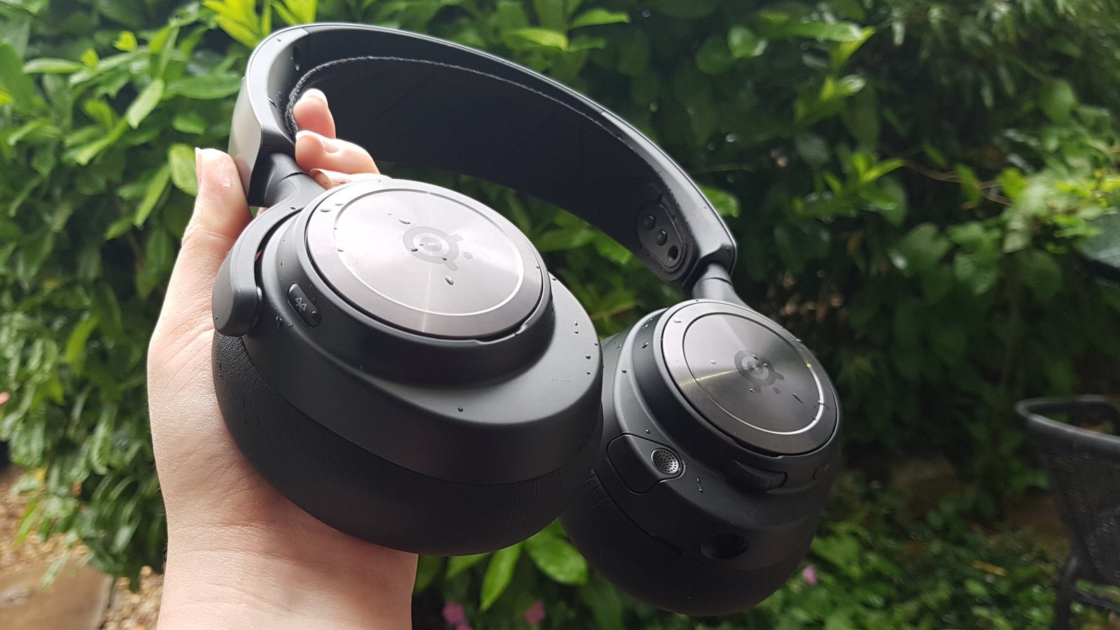 The SteelSeries Arctis Nova Pro wireless held up in front of a bush.